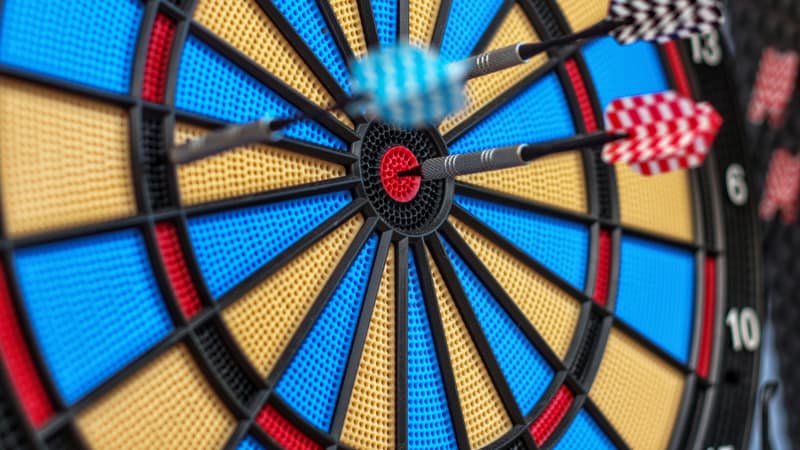 Colorful darts hit bullseye on dartboard, capturing precision and focus.
