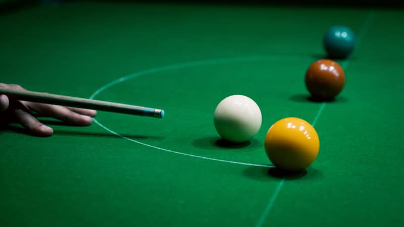 Focused shot of a snooker cue aiming at colored balls on a green table.